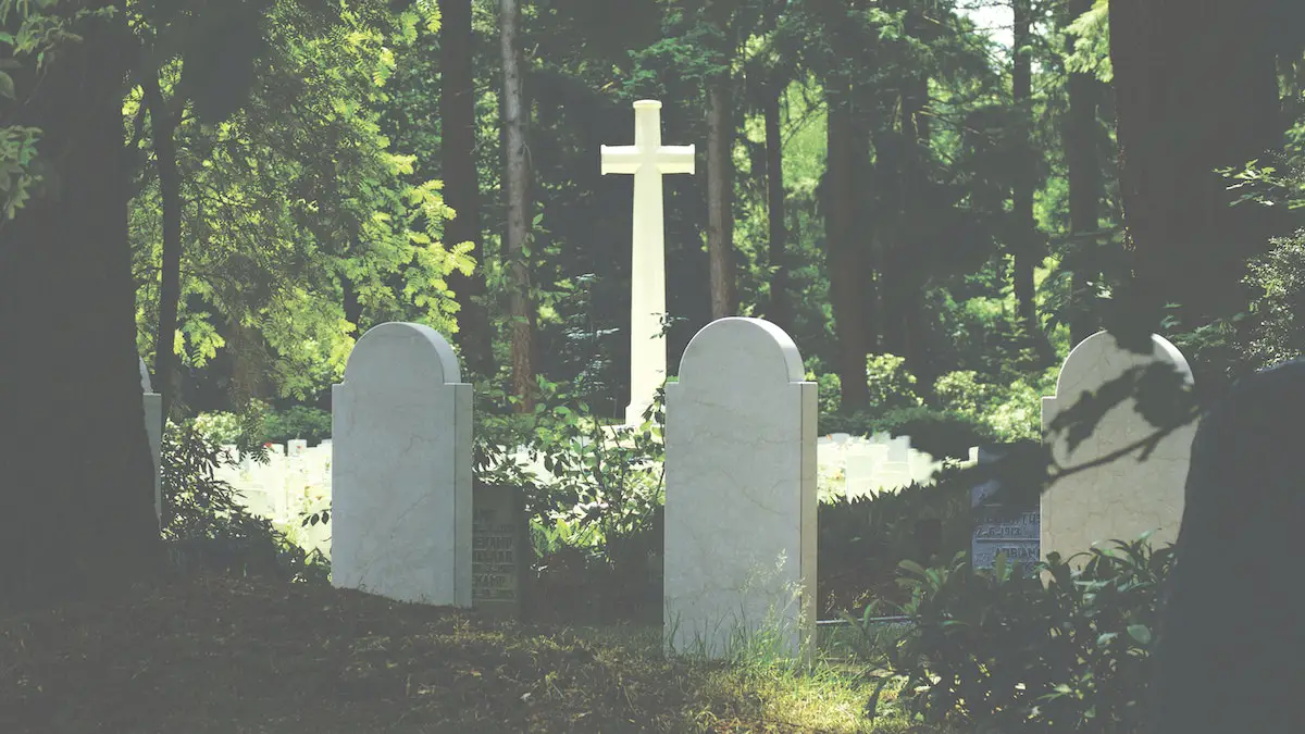 White Tombstone Near Cross Surrounded by Trees